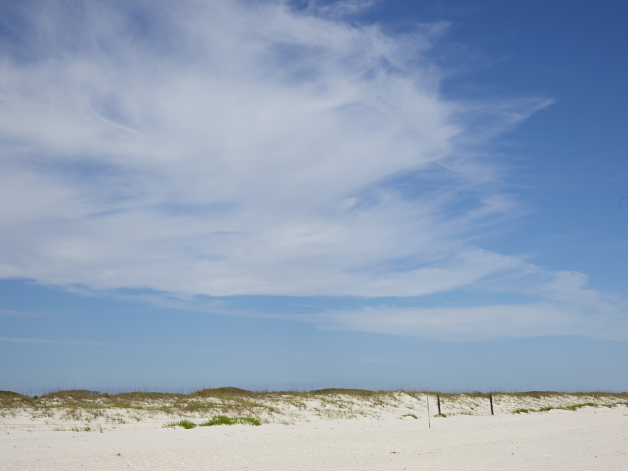 Landscape photo of a white beach stretching across the horizon, with blue skies and white clouds